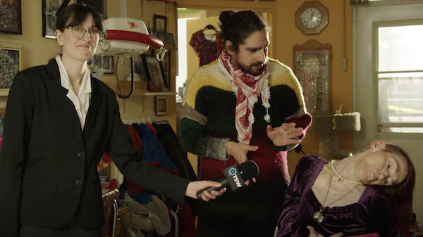 A reporter from the satirical news show The Squeaky Wheel: Canada is interviewing a non-verbal wheelchair user and her non-disabled assistant.