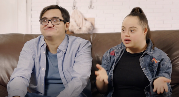 An intellectually disabled couple are shown seated on a couch talking to an off-screen reporter.