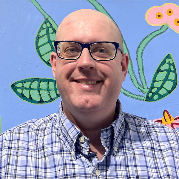 A headshot of the artist Aaron Harvey. He is a young man wearing glasses and a dress shirt, and smiling.