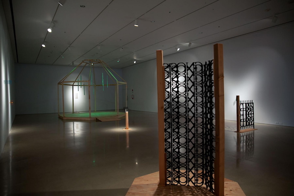 Installation view of AO Roberts' exhibition Sickroom at the University of Manitoba School of Art Gallery. There are two text-based sculptures in the foreground and one architectural installation in the background.