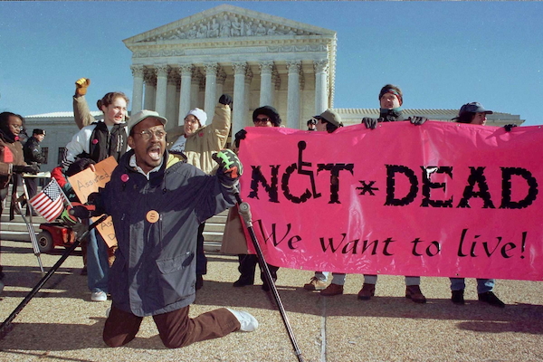 Archival image of a Black man leading a group of protesters in front of the Supreme Court, kneeling with his crutches outspread and his mouth mid-yell, while holding a small American flag. A neon pink banner to the right reads, “NOT DEAD. We want to live!”