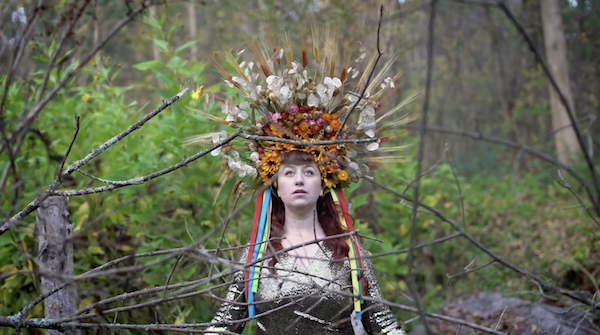 A figure standing in the forest wears a floral headdress in a scene from the short video Dreamscapes.