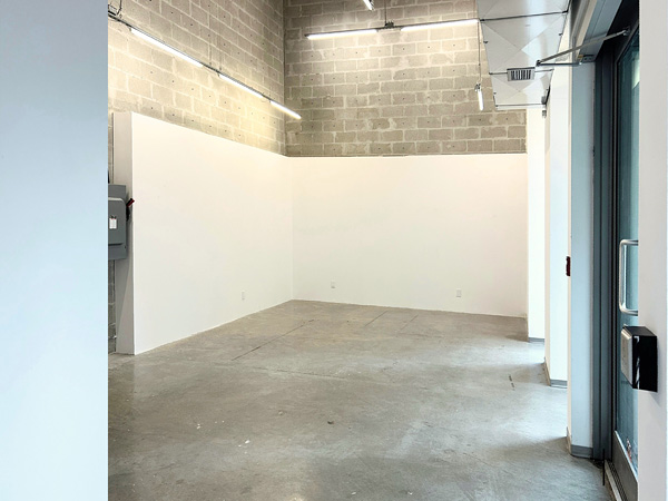 Interior of Gallery A: daylight from right (windows out of frame); white walls left/back; grey brick wall behind extends to ceiling.