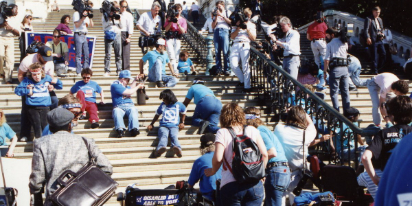A large protest in Washington, DC, from 1990, with a crowd of disabled activists crawling up the stairs of the Capitol Building.