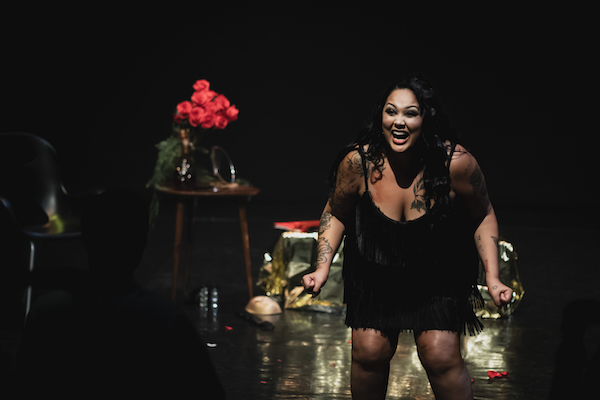 A woman on stage in a slip dress clenches her fists and screams toward the audience.