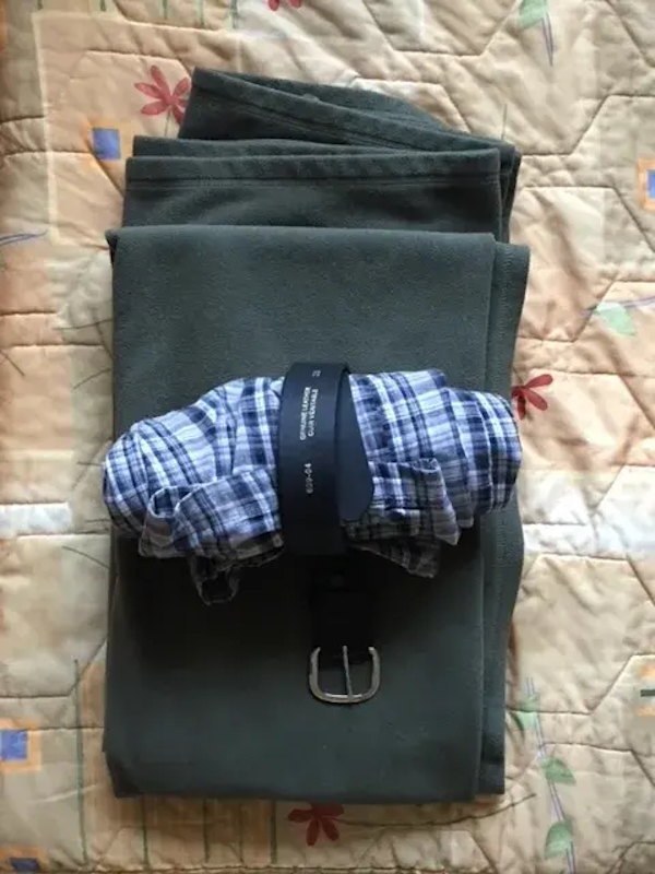 Pyjama bottoms rolled up and tied with a belt, on top of a folded blanket on top of a bedspread.