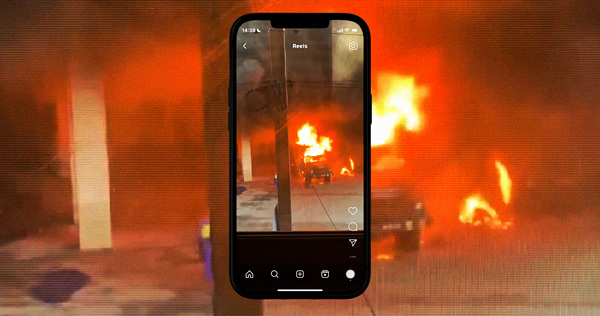 Production still from “The Longer You Bleed” showing a smartphone screen capturing a burning vehicle at night