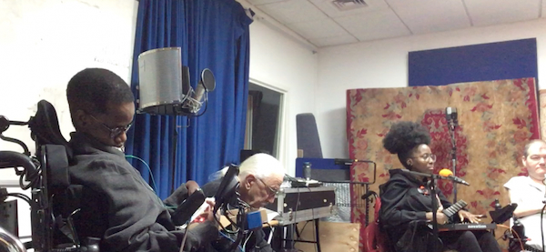 Three musicians seated in wheelchairs using a variety of musical instruments (though not all of them are visible).