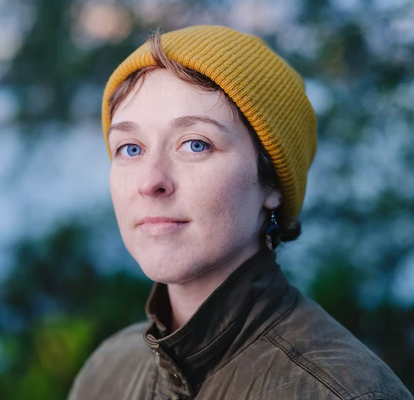 This portrait of Conyer Clayton depicts them smiling and wearing a mustard-coloured toque.