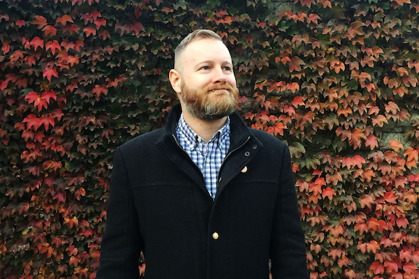 This portrait of Jim Johnstone depicts him smiling and standing in front of a vine-covered wall.