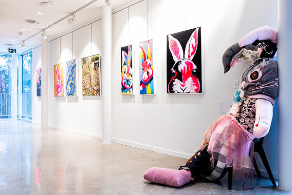 Large stuffed rabbit on a stool in a gallery with paintings on the walls