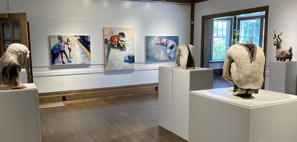 A gallery room with large sculptures on pedestals and three paintings on the wall