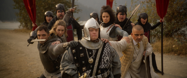 The cast of King Arthur's Night, dressed in battle armour, gather behind King Arthur and wield their swords. 