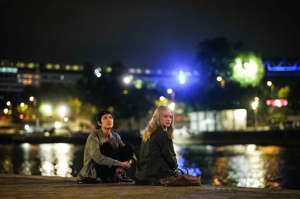Two young women sit together on an urban waterfront at night. This is a scene from the movie All of a Sudden.