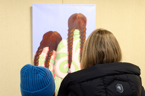 Two visitors viewing a colourful painting of two figures with long braids at the New Vistas exhibition.